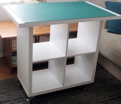 a white table with three shelves on it in front of a couch and coffee table