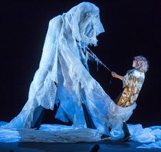 a man standing next to a giant white creature on top of snow covered ground in front of a black background