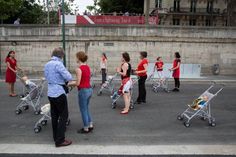 several people standing in the middle of a parking lot with carts full of luggage and one person pushing a stroller