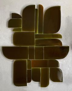 an abstract piece of art made out of brown and green glass tiles on a white wall