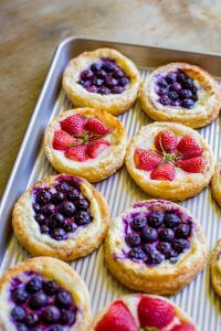 small pastries with berries and blueberries are on a baking sheet, ready to be baked