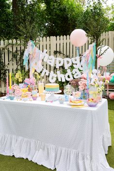 an outdoor birthday party with balloons, cake and decorations on a table in front of a white picket fence