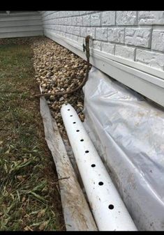 a white pipe laying on top of a grass covered ground next to a building with rocks in it