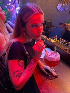 a woman sitting at a bar with a drink in her hand and tattoos on her arm