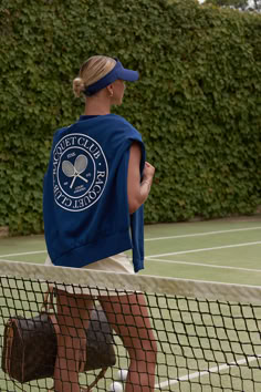 a woman with a tennis racket walks on the court while wearing a blue jacket