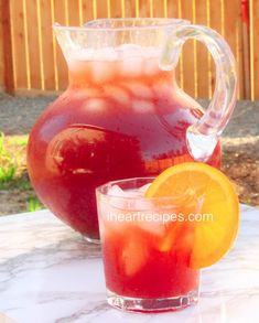 a pitcher and glass filled with liquid sitting on top of a marble table next to an orange slice