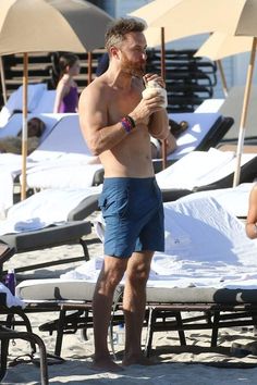 a shirtless man standing on top of a beach next to chairs and umbrellas