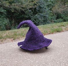 a purple crocheted hat sitting on top of a cement ground next to trees