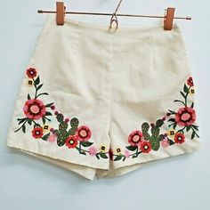 a pair of shorts with flowers on them hanging from a wooden hanger in front of a