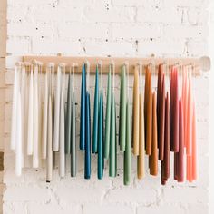 colorful candles are hanging on the wall in front of a white brick wall and wooden shelf