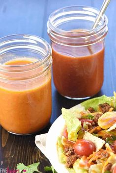 two mason jars filled with sauce and salad on top of a table next to a plate