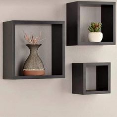 three black shelves with two vases and one plant on each shelf in front of the wall