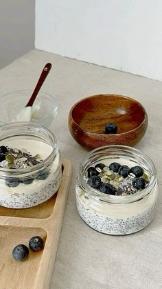 two jars filled with yogurt and blueberries on top of a cutting board