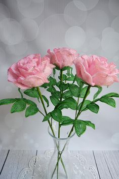 three pink roses in a clear vase on a white wooden table with polka dot background