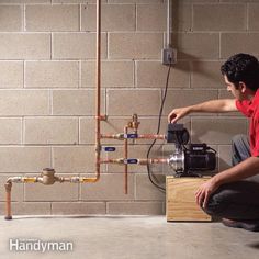 a man kneeling down in front of a water heater with pipes coming out of it