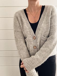 a woman wearing a gray cardigan sweater and black pants standing in front of a white wall