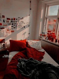 an unmade bed with red sheets and pictures on the wall behind it in front of a window