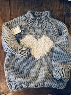 a knitted sweater with a white heart on the front and grey, off - white, and light blue colors