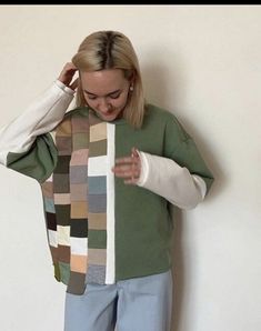 a woman standing in front of a white wall wearing a green sweater and blue pants