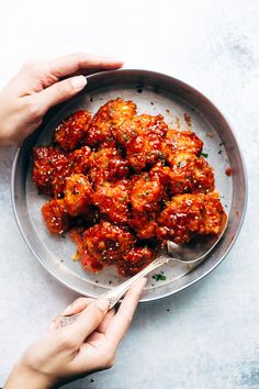 two hands holding a spoon over a plate of food with meatballs and sauce on it