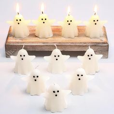 six candles with ghost faces on them are sitting in front of a wooden tray that holds five lit candles