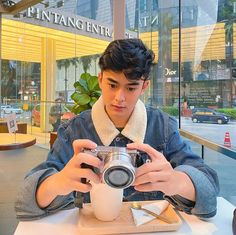 a man sitting at a table with a camera in front of him and holding a cup