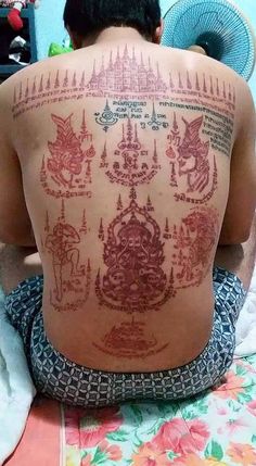 a man sitting on top of a bed with tattoos on his back and arms behind him