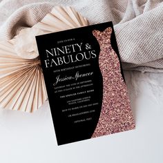 a black and gold wedding card with a pink dress on it next to a fan