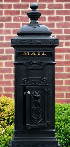 a black mailbox sitting in front of a brick wall and shrubbery with the word mail written on it