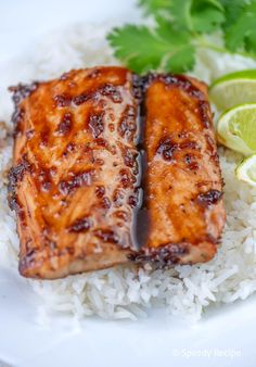 two pieces of salmon sitting on top of white rice next to limes and cilantro