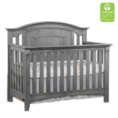 a gray crib with white sheets on the bottom and side rails, is shown in front of a white background