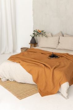 a bed with an orange blanket on top of it next to pillows and a plant