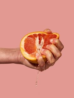 a person's hand holding an orange slice with water coming out of the end