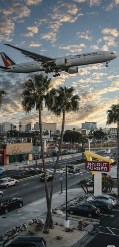 an airplane is flying over a busy street with palm trees and buildings in the background