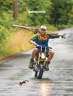 a man riding on the back of a motorcycle down a rain soaked road next to a squirrel