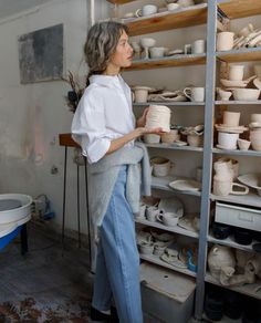 a woman standing in front of shelves filled with pottery