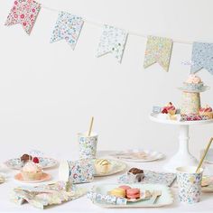 a table topped with cakes and cupcakes next to bunting flags on a white wall