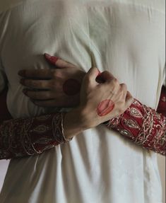 a woman in white dress holding onto her arm with red and gold bracelets on it