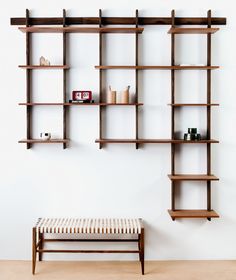 a wooden shelf with several shelves on it and a bench in the foreground, against a white wall