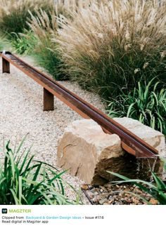 a wooden bench sitting in the middle of a garden next to tall grass and plants