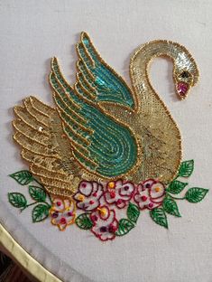 a close up of a embroidery on a white cloth with flowers and a gold swan