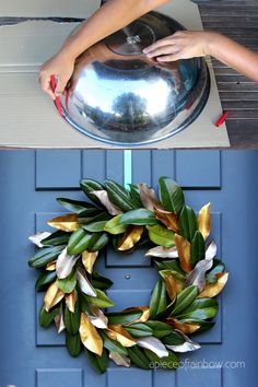 a wreath made out of fake leaves on top of a blue door with a hand reaching for it