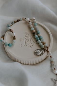 a white tray with some beads and a silver charm on it's side, sitting on a white cloth