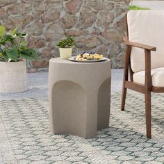 a chair and table sitting on top of a rug next to a stone wall with potted plants