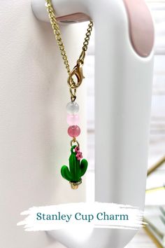 a small cactus charm hanging from a gold plated metal hook on a white wall