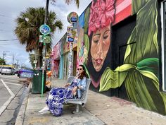 a woman sitting on a bench in front of a mural