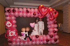 a couple standing in front of a heart shaped balloon frame with balloons attached to it