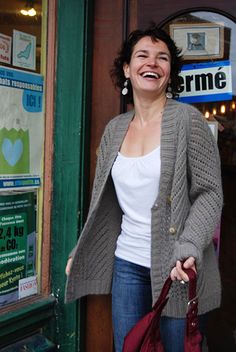 a smiling woman holding a red purse in front of a storefront with posters on the door