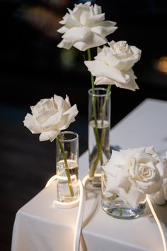 three vases with white flowers in them on a table next to two glasses filled with water