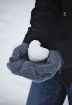 a person holding a snowball in their hand on a snowy day with blue jeans and black jacket